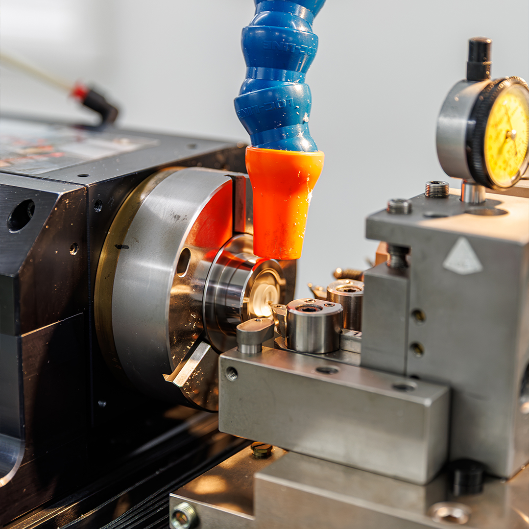 Close-up of a precision manufacturing machine producing a small metal component, with coolant directed onto the cutting area.