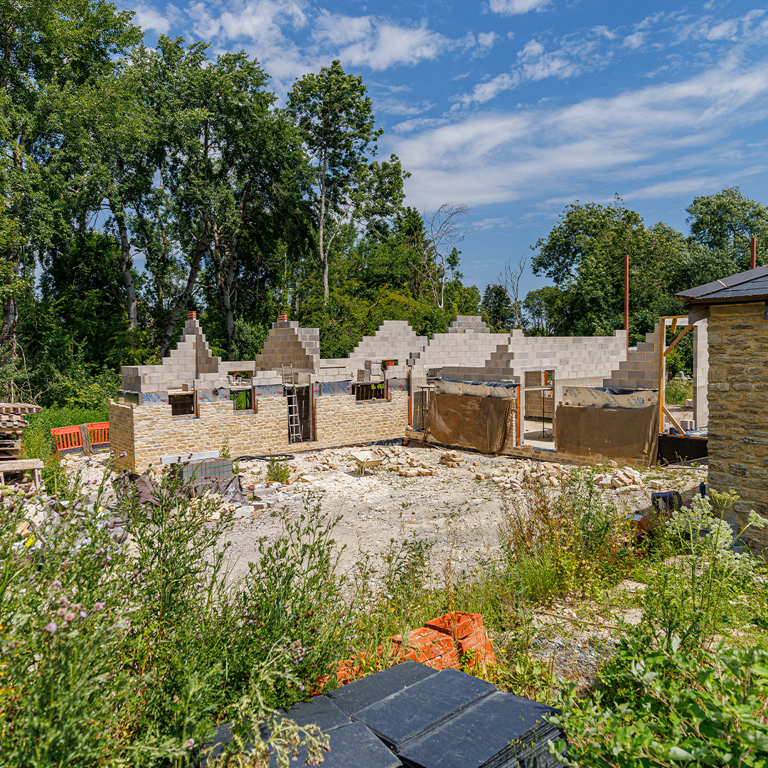 Ground-level view of a new-build property under construction, showing stone walls, concrete blockwork and partially completed gable ends.