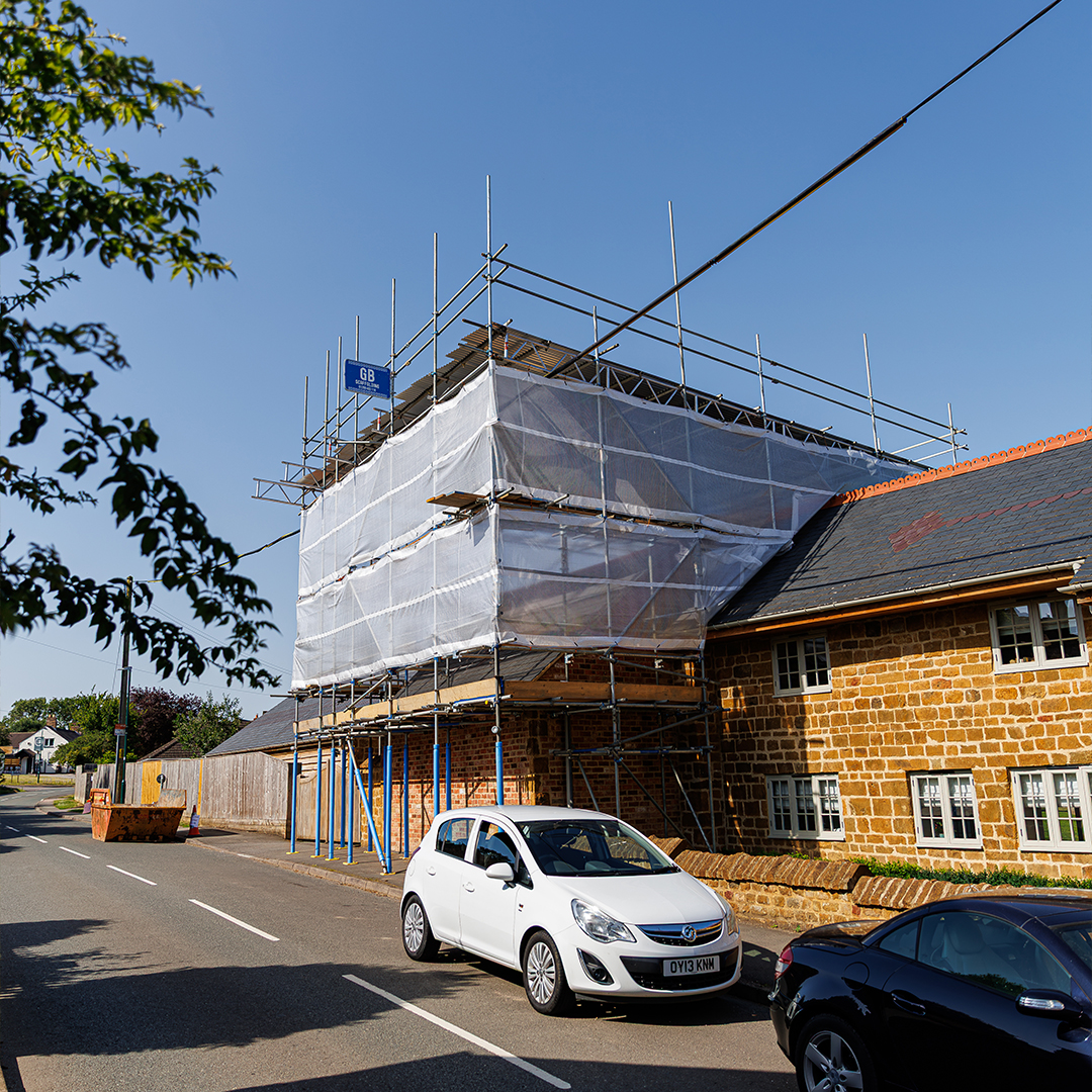 Street-level view of scaffolding and protective sheeting surrounding a stone property during roof and building renovation work.